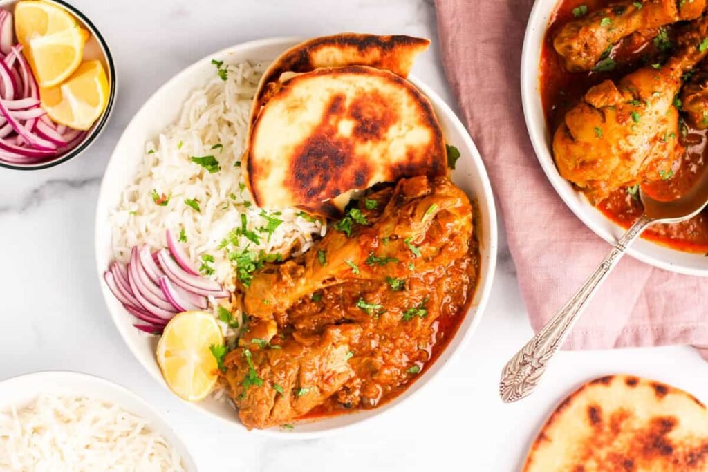 chicken korma served in a white bowl with naan and rice