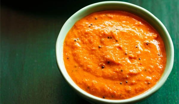 onion chutney in a green bowl with dosa stacked on a white plate on a dark green board